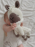  baby holds  a stuffed alpaca toy in neutral colours.