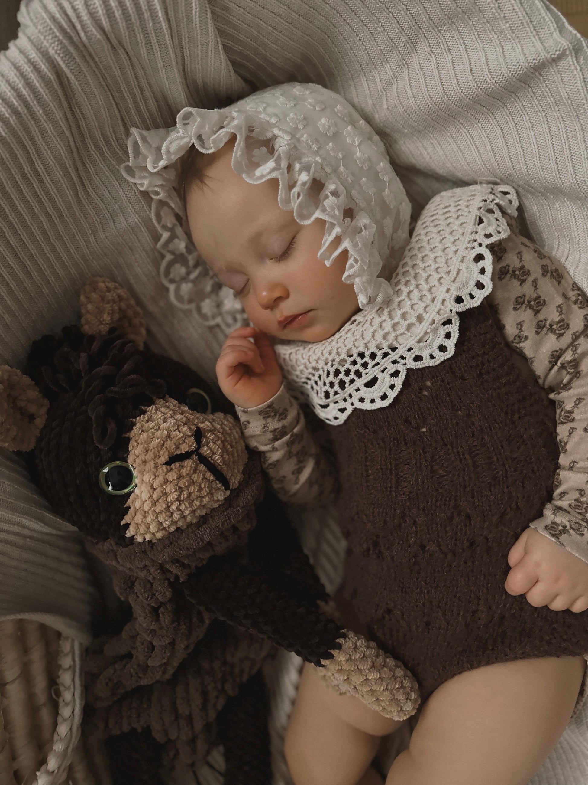  baby laying on a bed next to a stuffed alpaca toy in brown colours.